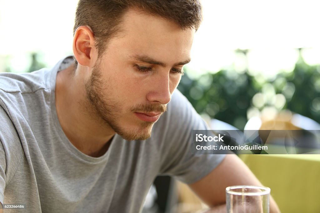 Sad man drinking in a bar Portrait of a very sad single man sitting alone and drinking outside in a restaurant terrace Men Stock Photo