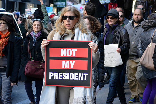 New York City New York, New York - November 12, 2016: Protester carrying a sign while marching in a "Trump is not my President" rally in response to the 2016 Presidential Election of Donald Trump in New York City in 2016. donald trump stock pictures, royalty-free photos & images