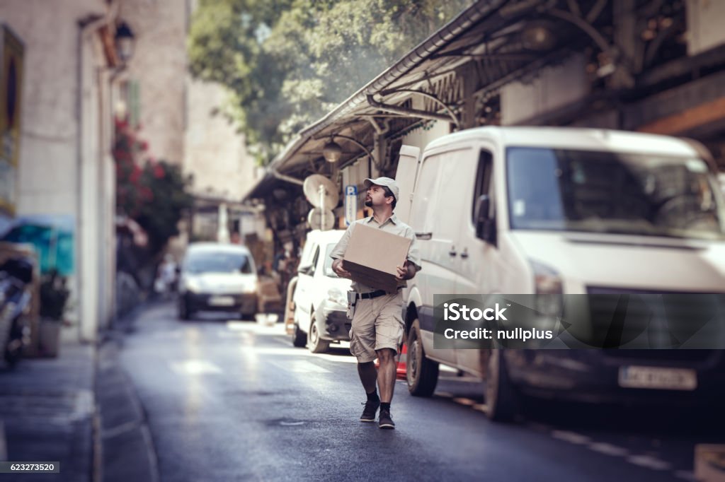 Messenger delivering parcel, walking in street next to his van City Stock Photo