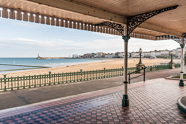 Margate Bay from a victorian shelter in Kent, England. Margate Bay from a victorian shelter in Kent, South-east England, UK. It is an arching bay with a coast path running next to the shoreline. Part of margate town and harbour is visible in the distance. Victorian railings also line the beach front. kent england photos stock pictures, royalty-free photos & images