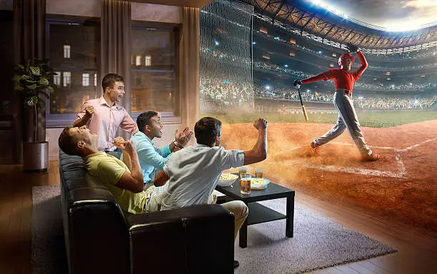 :biggrin:A group of young male friends are cheering while watching extremely realistic Soccer game at home. They are sitting on a sofa in the modern living room faced to a real stadium with players instead of the front wall. It is evening outside the window.