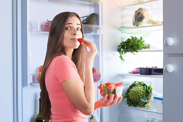 istock young beautiful woman eating strawberries from the fridge 623279680