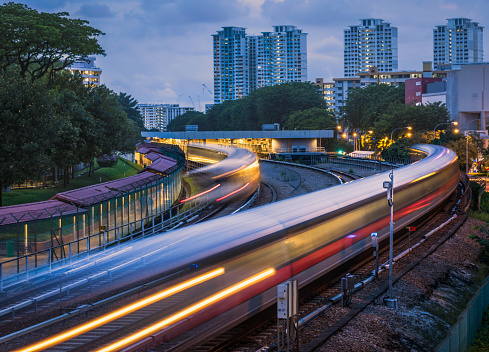 Mass Rapid Transit (MRT) trains arriving and leaving the station of Ang Mo Kio in Singapore. The image was taken in the evening during blue hour and the trains have motion blur.