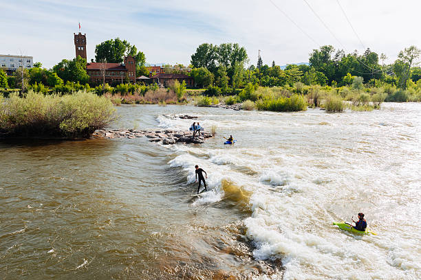 People Surf and Kayak Brennan's Wave in Missoula Montana USA Missoula, United States - May 13, 2016: People wearing wetsuits surf and kayak on a man made wave, Brennan's Wave, in the Clark Fork River that runs through the center of the Montana town. missoula stock pictures, royalty-free photos & images