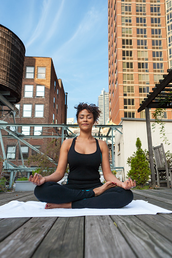 Young african American woman practicing yoga on a rooftop garden in NYC. the quarte lotus position.