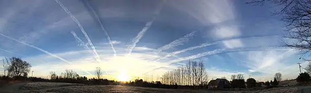 Jet trails fill the morning sky, converging on the sunrise.