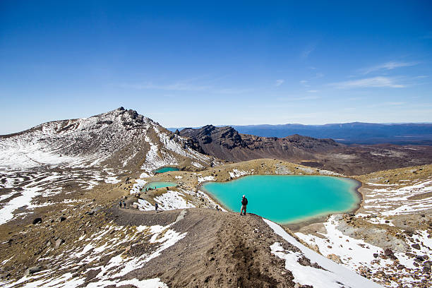 Hiker watching over emerald lakes Tongariro Alpine, New Zealand - October 13, 2013: Hiker standing and watching over the emerald colored lakes of the Tongariri Alpine Crossing in New Zealand.  tongariro national park photos stock pictures, royalty-free photos & images