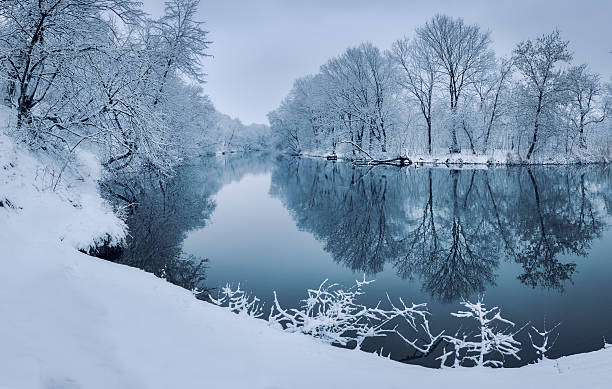 Colorful landscape with snowy trees, beautiful frozen river at sunset Winter forest on the river at sunset. Colorful landscape with snowy trees, beautiful frozen river with reflection in water. Seasonal. Winter trees, lake and blue sky. Frosty snowy river. Weather snow river stock pictures, royalty-free photos & images