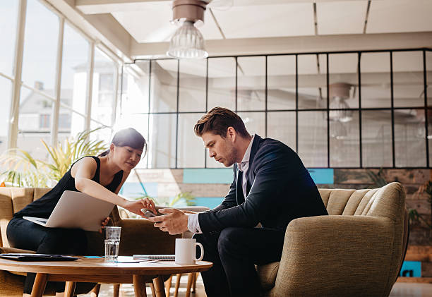 istock Two people sitting in office lobby using mobile phone 623348668