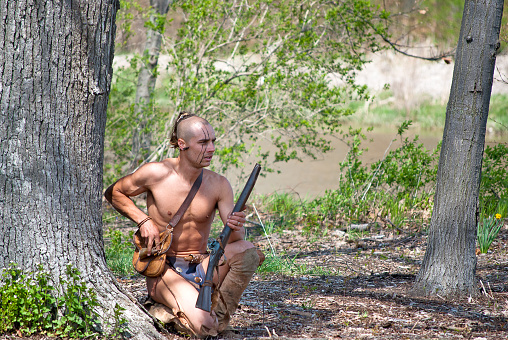 Indian warrior with gun in woods by river