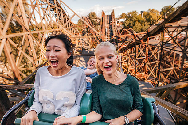 Young friends riding roller coaster ride Shot of young friends riding roller coaster ride at amusement park. Young people having fun at amusement park. rollercoaster stock pictures, royalty-free photos & images