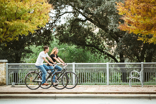A cute couple in their mid 40's ride some cruiser bicycles around downtown Austin Texas, taking in the views and autumn foliage of the city.  Horizontal image with copy space.