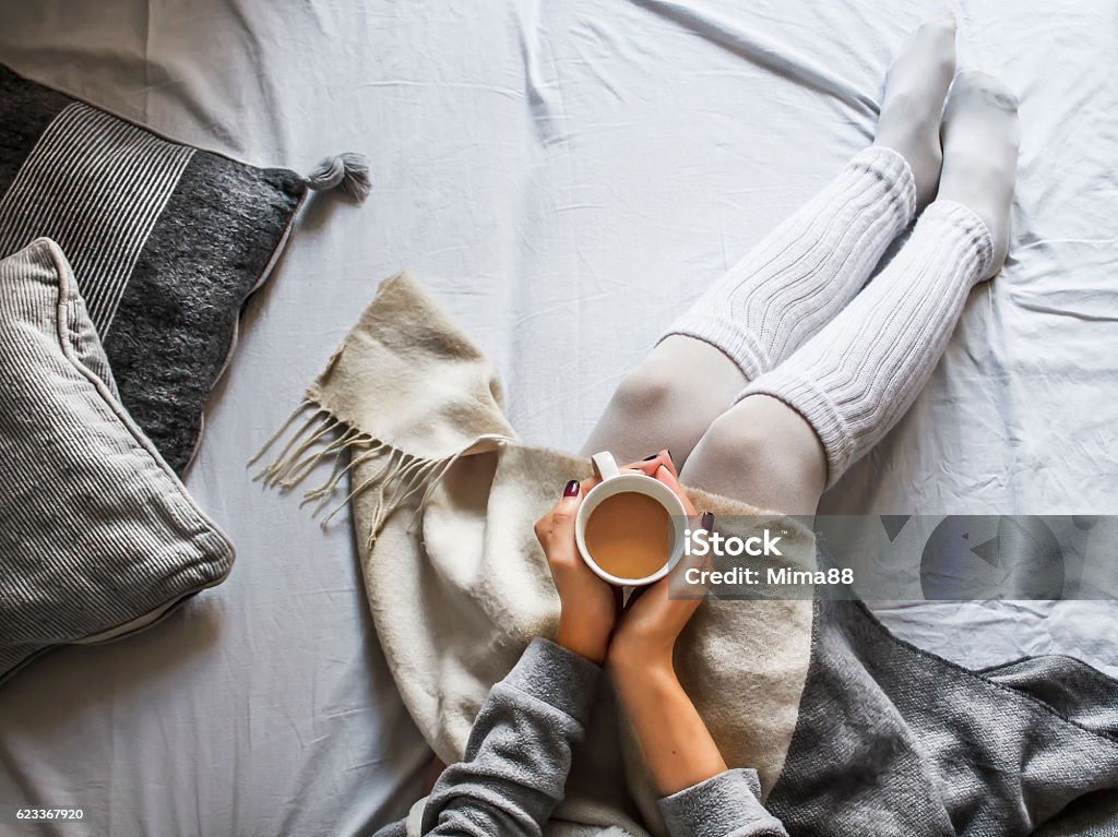 young woman on a bad holding a cup of coffee young woman sitting on a bad holding a cup of hot coffee on a cold winter morning at home Winter Stock Photo