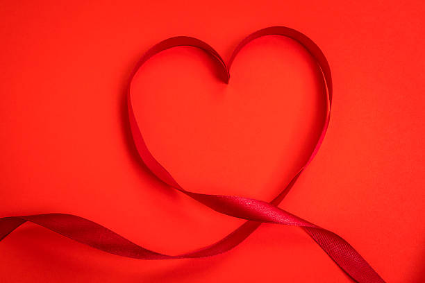 istock Red ribbon making the shape of heart on red background 623373462