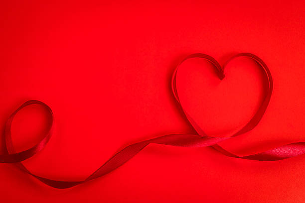 istock Red ribbon making the shape of heart on red background 623373478