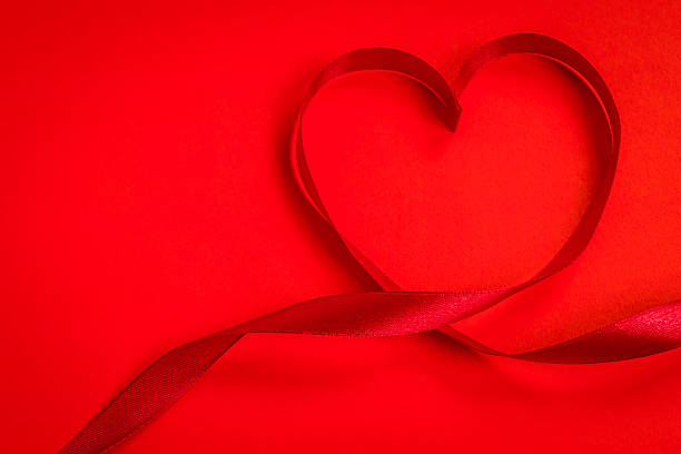 istock Red ribbon making the shape of heart on red background 623373496