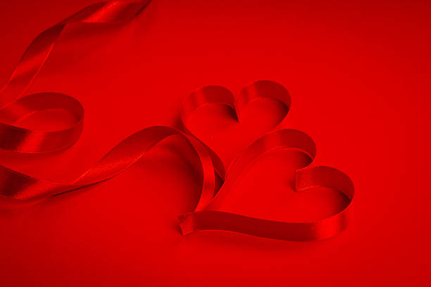 istock Red ribbon making the shape of heart on red background 623374154