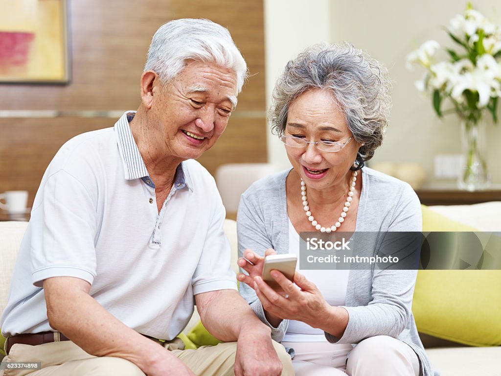 senior asian couple using cellphone at home happy senior asian couple looking at mobile phone at home, happy and smiling Senior Adult Stock Photo