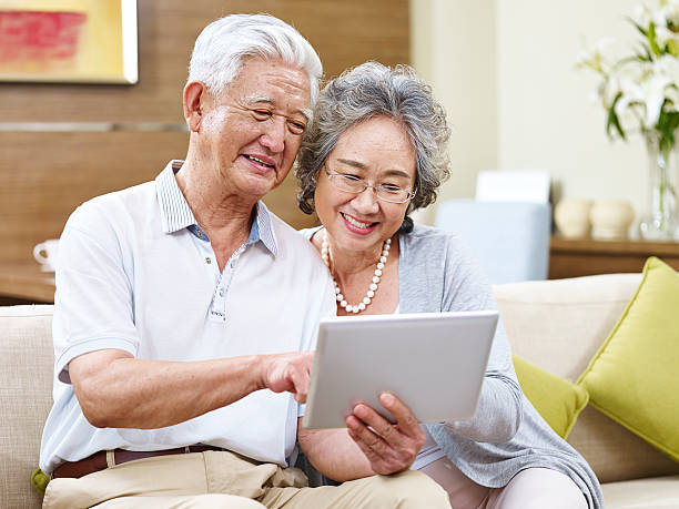 coppia asiatica senior utilizzando un tablet insieme - ipad senior adult facebook sofa foto e immagini stock