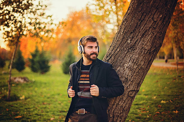 istock Hipster with headphones leaning on the tree in park 623380452