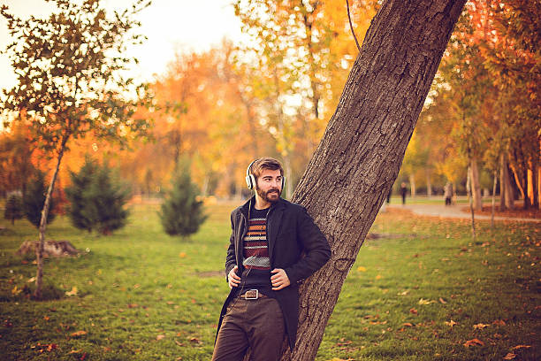 istock Hipster with headphones leaning on the tree in park 623380508