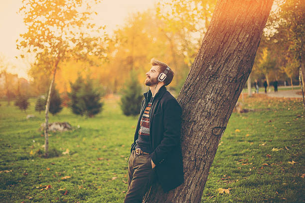 Hipster with headphones leaning on the tree in park