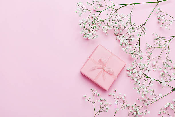 Gift or present with flowers on pink table. Flat lay.