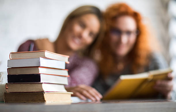 Stack of books on the table with people in background.