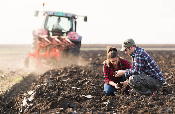 トラクターが畑を耕している間に汚れを試験する農家 - plowed field dirt agriculture field ストックフォトと画像