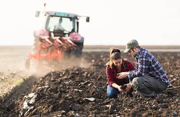 Photo of Farmers examing dirt while tractor is plowing field