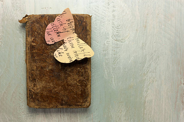 A photo of an old book with a butterfly cut out of paper toned with watercolor, shot from above on a wooden board, with copyspace