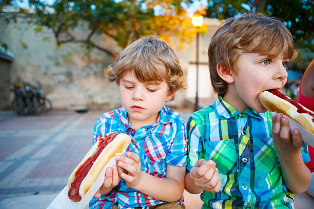 dois meninos comendo cachorros-quentes ao ar livre - food picnic hot dog unhealthy eating - fotografias e filmes do acervo