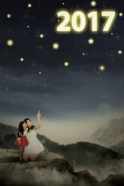 Picture of young mother embracing her daughter while pointing numbers 2017 at the night sky