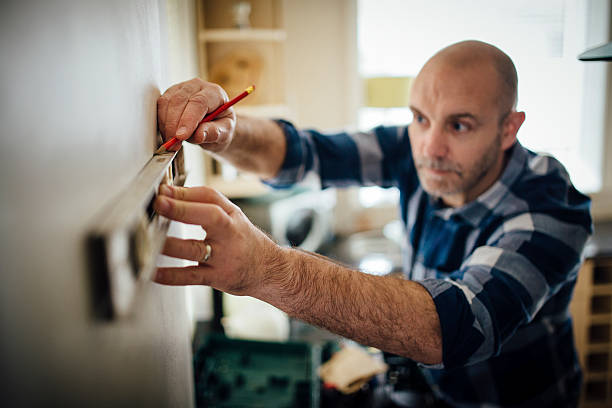 DIY in the Kitchen Mature man using a spirit level and marking the wall with a pencil in his kitchen. spirit level stock pictures, royalty-free photos & images