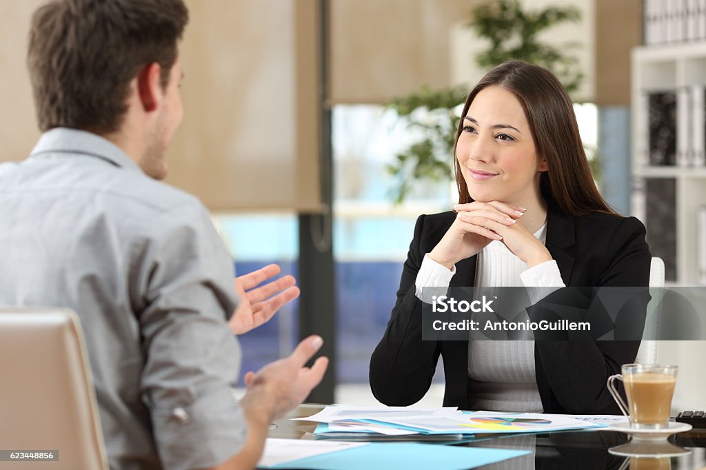 Businesswoman attending a client at office Businesswoman attending listening to a client who is talking at office Interview - Event Stock Photo