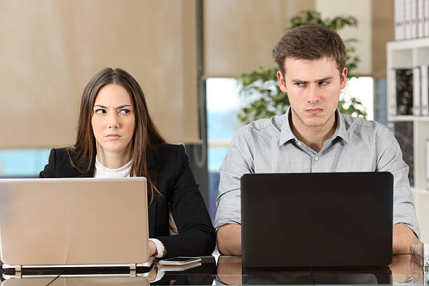 Two angry businesspeople disputing Front view of two angry businesspeople using computers disputing at workplace and looking sideways each other with envy displeased stock pictures, royalty-free photos & images