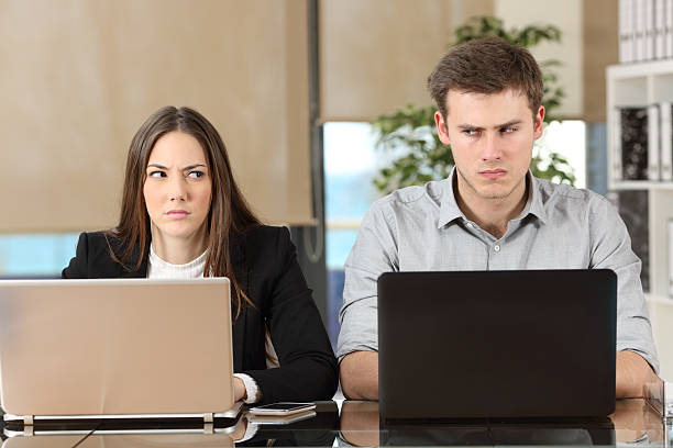 Two angry businesspeople disputing Front view of two angry businesspeople using computers disputing at workplace and looking sideways each other with envy Displeased stock pictures, royalty-free photos & images