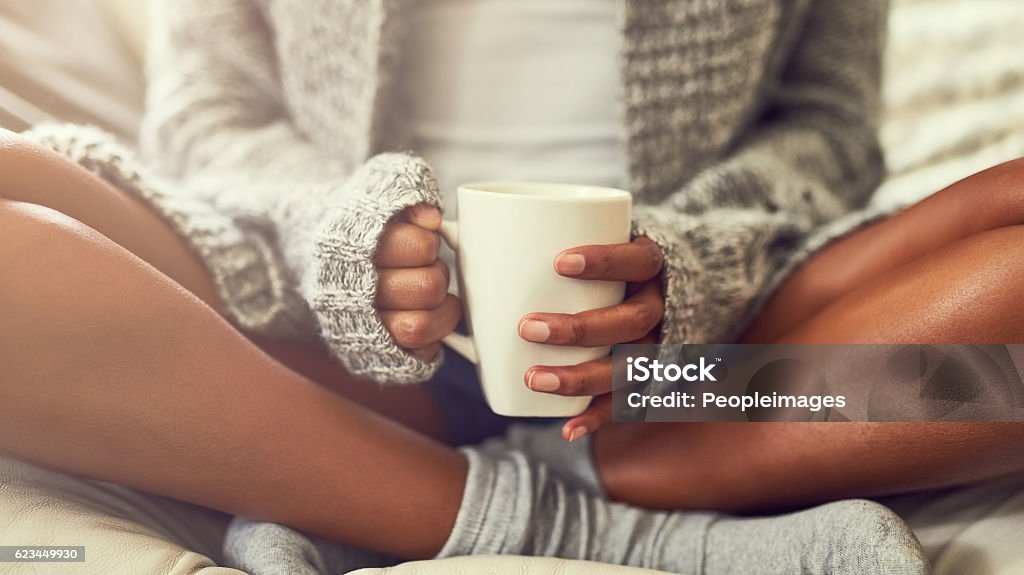 Weekend bliss Shot of an unidentifiable young woman enjoying a cup of coffee while sitting on her couch at home Tea - Hot Drink Stock Photo