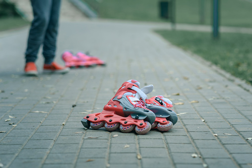 pink children's roller skates lying on the footpath against the background of legs