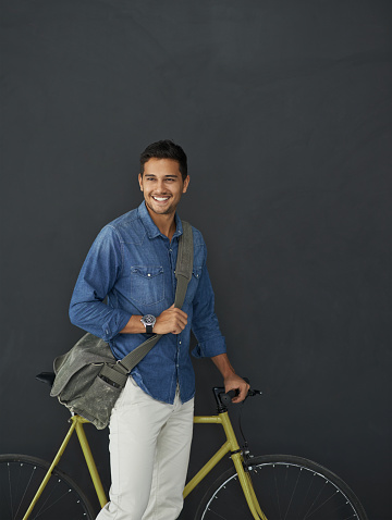 Studio shot of a handsome young man posing with his bicycle against a grey background