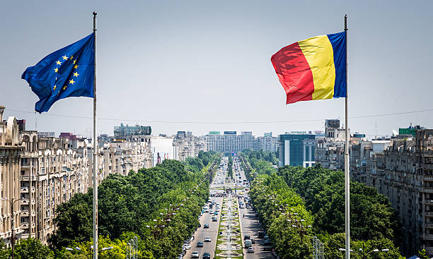 Romanian and European Union flag flying in Bucharest, Romania Close up image of the Romanian flag and the European Union (EU) flags flying at the top of the Palace of Parliament in Bucharest, Romania. In the distance we can see the main street of Bucharest stretching out into the distance, flanked by green trees and thronged with busy afternoon traffic. Horizontal colour image with copy space. bucharest photos stock pictures, royalty-free photos & images