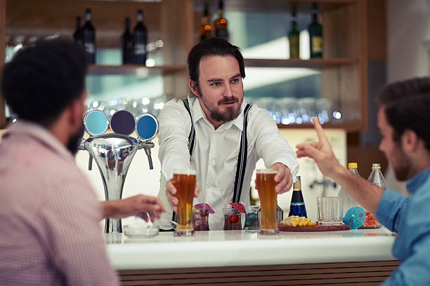 To quench your thirst Shot of a friendly barman serving beer to two customers at his bar quench your thirst pictures stock pictures, royalty-free photos & images