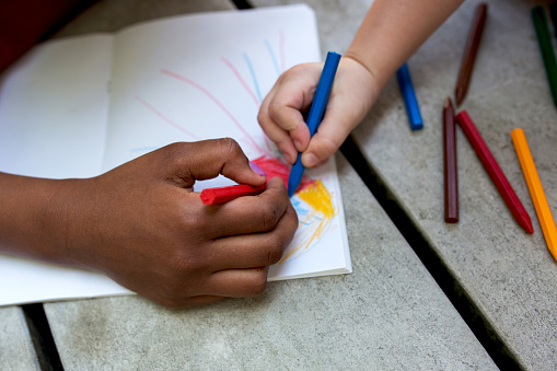 Close up of two unrecognizable children coloring together with crayons.