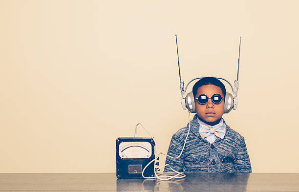 Young Boy Dressed as Nerd with Alien Headphones A young boy imagines reading mind and receiving communications from outer space with a homemade science project on his head. He is dressed in casual clothing, glasses and bow tie. He is wearing headphones in front of a beige background with a serious expression waiting. Retro styling. science and technology kids stock pictures, royalty-free photos & images