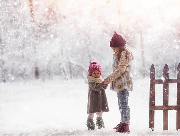 Two cute children girls playing on a winter walk in nature. Happy kids outdoors.