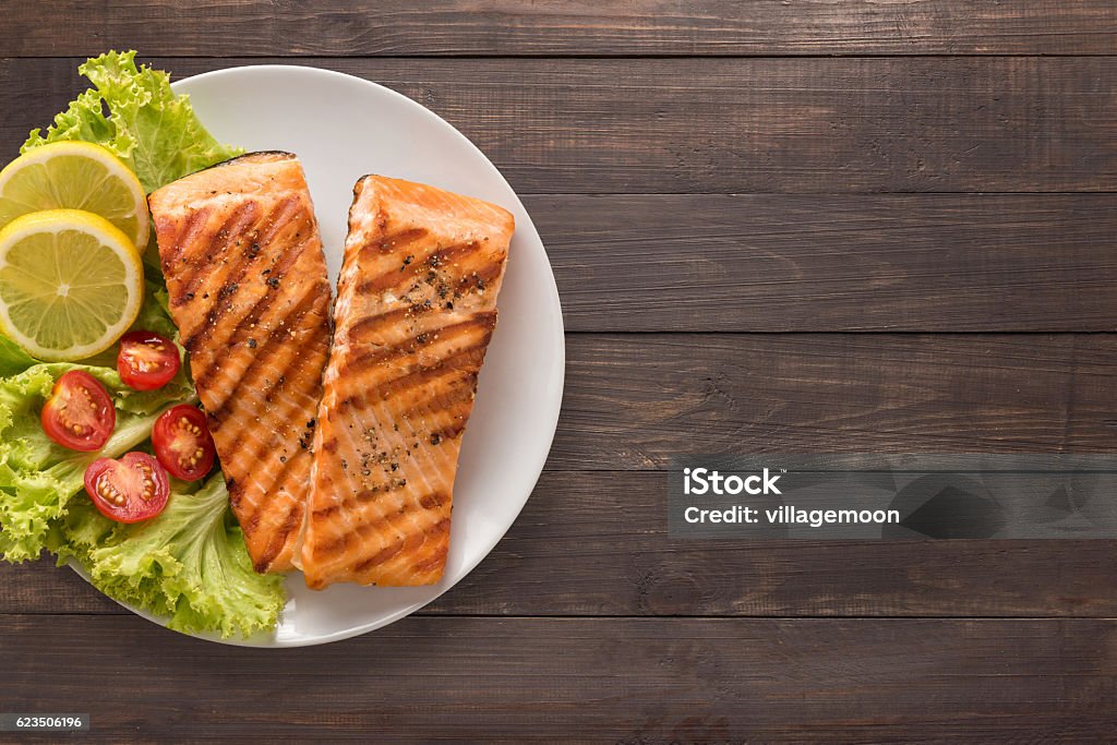 Grilled salmon with lemon, tomato on the wooden background. Grilled salmon with lemon, tomato on the wooden background. Copyspace for your text. Salmon - Seafood Stock Photo