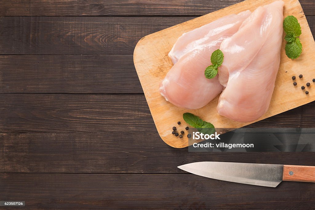 Top view raw chicken on cutting board on wooden. Top view raw chicken on cutting board and knife on wooden background. Copyspace for your text. Raw Food Stock Photo