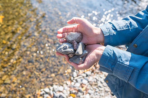 Embracing the tranquil beauty of the beach, a woman holds a heart-shaped stone with both hands above the sea. In this heartfelt moment, she connects with nature's rhythm, finding serenity by the shore. Close-up.