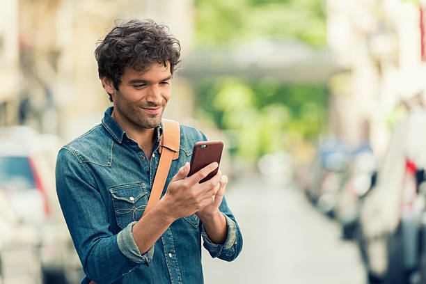 Cheerful male in the street texting on Mobile phone. Connected man in the street texting on app cell phone. Connection device. Texting, sms, chat, mail city of mobile stock pictures, royalty-free photos & images