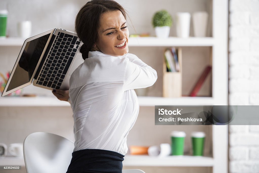 Stress concept Portrait of furious young woman about to throw and break her laptop at workplace. Stress concept Furious Stock Photo